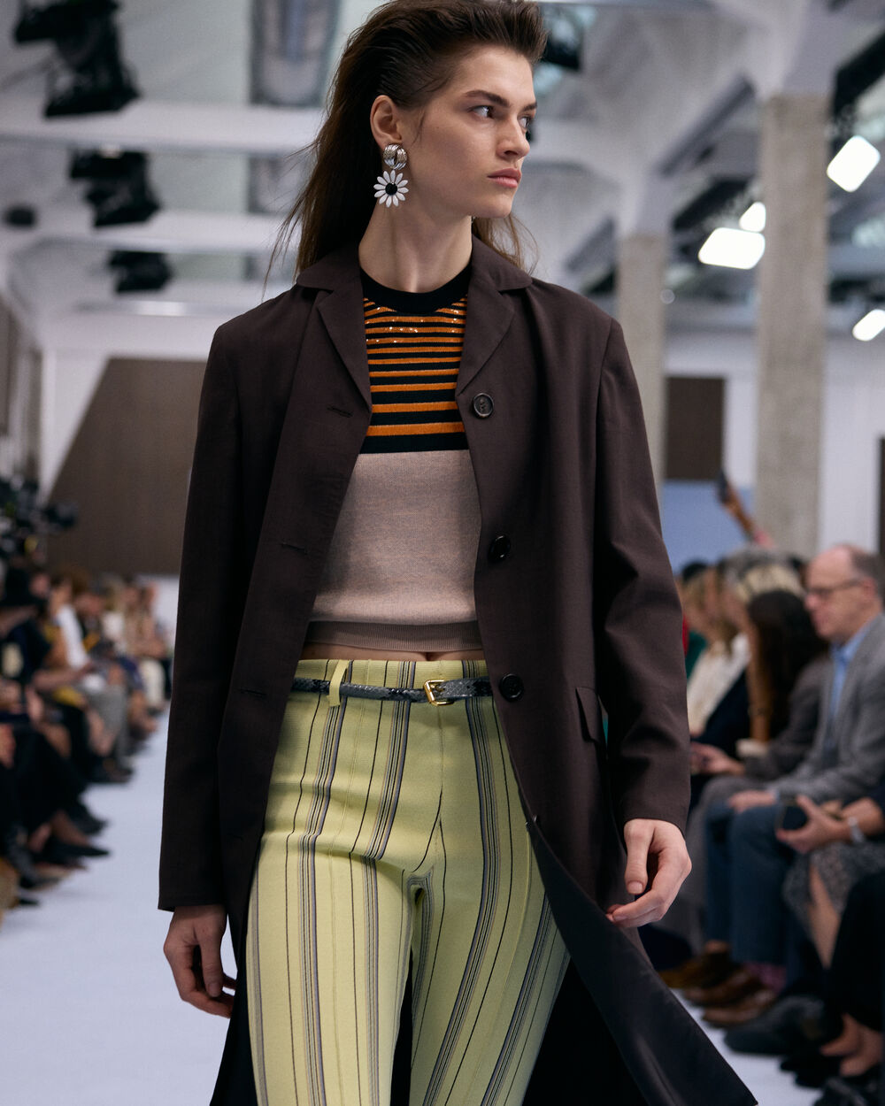 Model wearing a dark brown blazer, striped knit top and green trousers